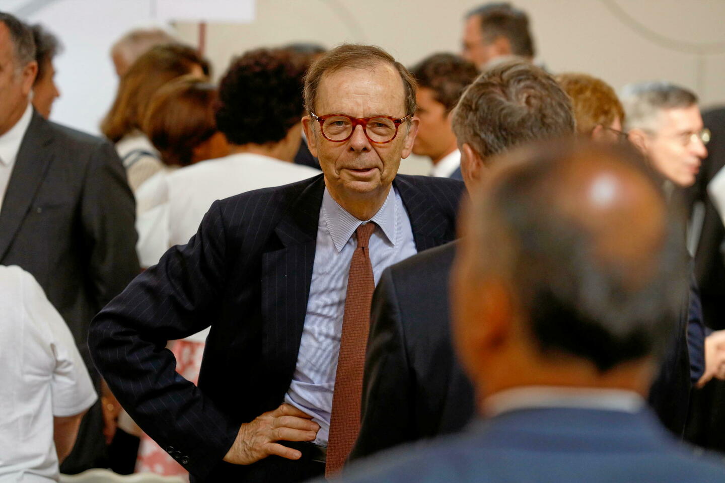 Louis Schweitzer en costume et cravate se tient debout dans une foule, affichant une expression sérieuse et concentrée.
